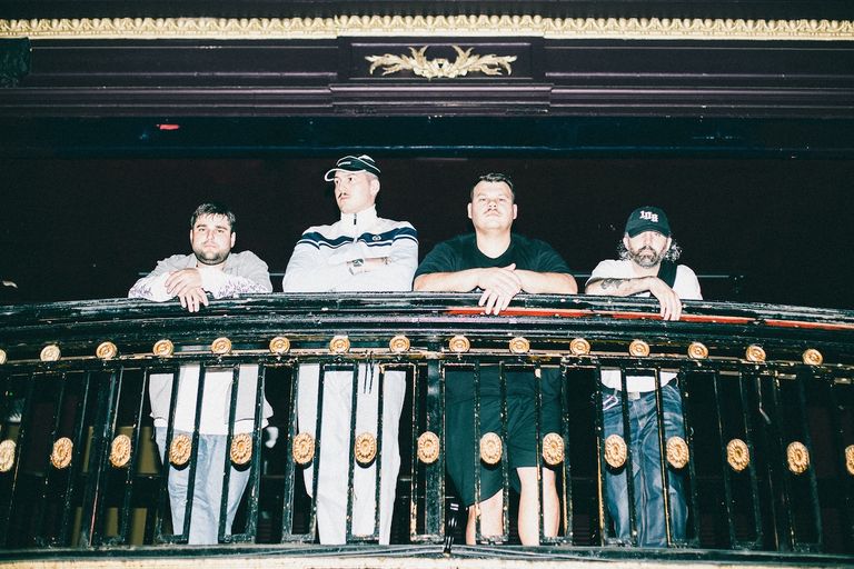 Australian rock band Trophy Eyes band members standing together and leaning on an ornate balcony railing inside a dark concert venue.